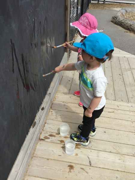 infants painting on outdoor chalkboard